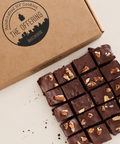 A close-up of chocolate cookie bars topped with chopped walnuts, arranged next to a kraft paper box printed with the brand name 'The Offering Bakehouse'.
