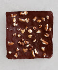 A square chocolate bar topped with chopped walnuts, photographed from directly above on a light gray background.