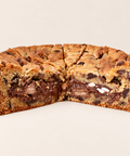 A chocolate chip cookie cut into wedges, with one slice cut open to show the thick cookie batter and melted chocolate filling, on a plain light beige background.