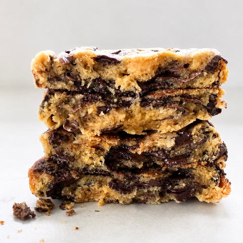 Three stacked chocolate chip cookie bars with melted chocolate chips, photographed close-up on a light neutral background.