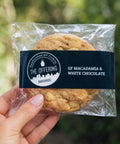 Cookie in clear packaging with 'The Offering Bakehouse' label, held by a hand against a blurred green background.