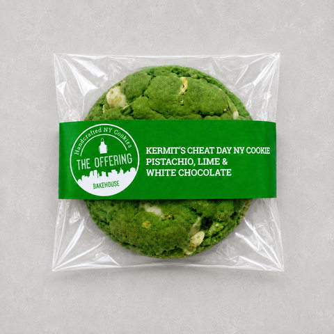 A packaged pistachio, lime, and white chocolate cookie from The Offering Bakehouse, sealed in a clear plastic bag with a green paper label.