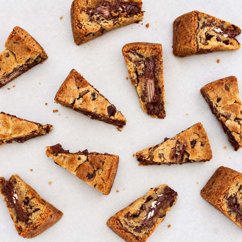 Several triangular chocolate chip cookie slices with melted chocolate filling are arranged on a light neutral background.