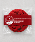 A packaged round cookie on a light gray background. The cookie is sealed in a clear plastic bag with a dark red paper band label.