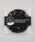 A packaged chocolate chip cookie from The Offering Bakery, featuring a black paper label with white text that reads "Pâté in the Puku" NY COOKIE WHITE CHOCOLATE & DRIED RASPBERRIES. The cookie is visible through a clear plastic bag on a light gray background.