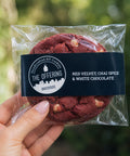 Packaged red velvet cookies with a visible brand label held by a hand against a blurred green background.