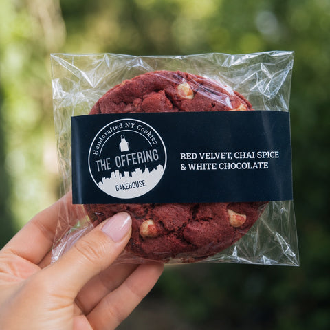Packaged red velvet cookies with a visible brand label held by a hand against a blurred green background.