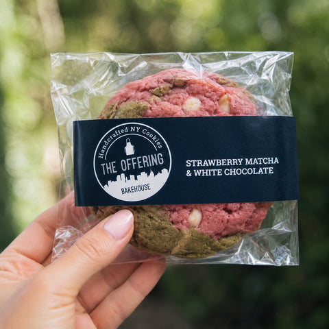 Packaged strawberry matcha and white chocolate cookies held by a hand with a blurred green background