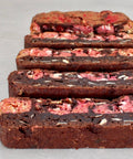 Four slices of a chocolate cookie or biscuit with pink strawberry filling and white chocolate chips, arranged on a light gray surface.