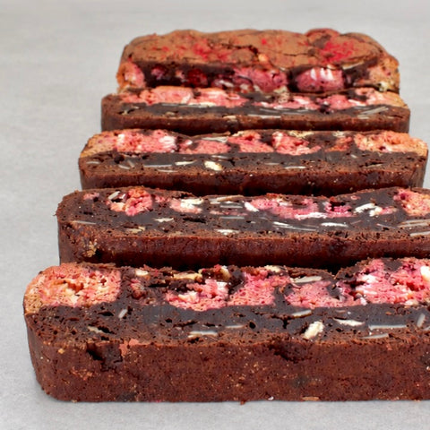 Four slices of a chocolate cookie or biscuit with pink strawberry filling and white chocolate chips, arranged on a light gray surface.