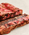 A close-up of a sliced chocolate chip cookie with pink fruit filling, likely strawberry, on a light gray surface.