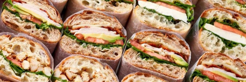 Close-up of multiple sliced sandwich wraps filled with chicken, avocado, tomato, and greens, arranged tightly together.