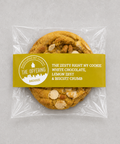A packaged cookie from The Offering Bakehouse, sealed in clear plastic with a yellow label. The cookie is golden brown with visible white chocolate chips and biscuit crumb pieces.